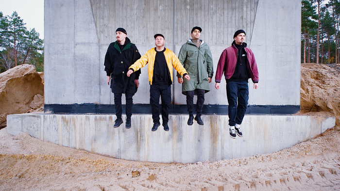 Vier Männer in Winterjacken posieren auf Betonstruktur.