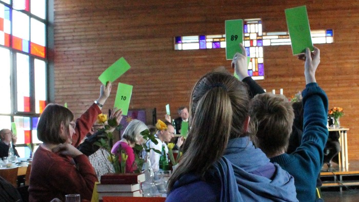 Eine Gruppe von Menschen hält grüne Pappsterne in einem Raum mit Backsteinwänden.