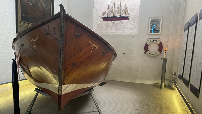 Ein hölzernes Boot und eine Rettungsweste in einem Raum mit Seekarten und einem runden Tisch.