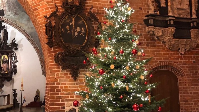 Ein festlich geschmückter Weihnachtsbaum vor einem Ziegelmauerwerk mit einem alten Spiegel.