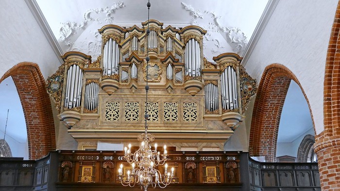 Große Kirchenorgel mit filigranem Design und Kronleuchter darunter