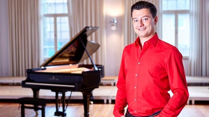 Mann in rotem Hemd vor Klavier in hellem Raum