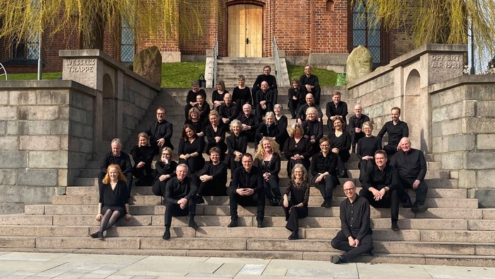 En gruppe korister poser på trin i forgrunden af en kirke