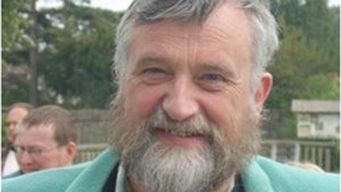 En smilende, eldre mand med grå bart og grøn jacke.