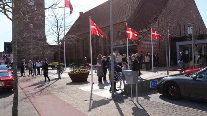 En gruppe af mennesker står udenfor et bygning med danske flag.