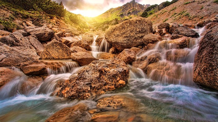 Ein Wasserfall fließt durch ein felsiges Gebirge bei Sonnenuntergang