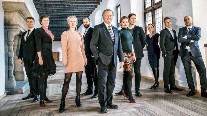 En gruppe formelt klædte erhvervsfolk står sammen i et historisk miljø.