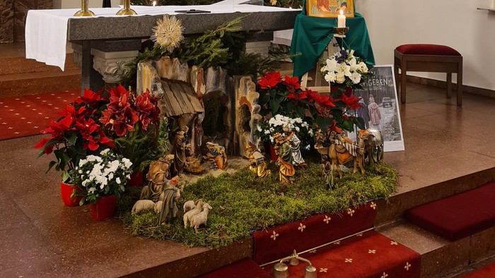 In der Kirche steht ein geschmückter Weihnachtsbaum mit Krippenfigur.