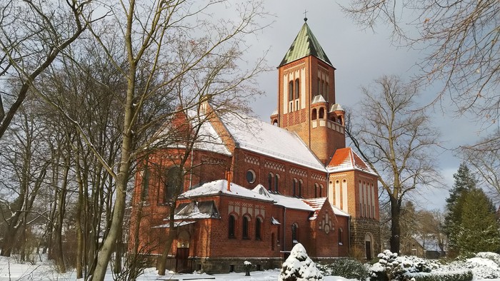 Ein rotes Backsteingebäude mit grünem Turm steht im Schnee, umgeben von kahlen Bäumen