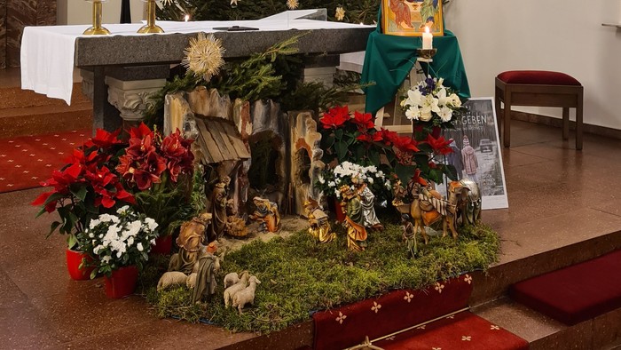 In der Kirche steht ein geschmückter Weihnachtsbaum neben einem Krippenszene-Diorama.