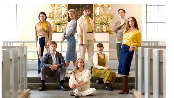 En gruppe af syv personer poserer på en trappe, alle klædt i farverne guld og blå