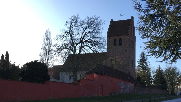 En kirke med tårn og en rød mur ved en vej