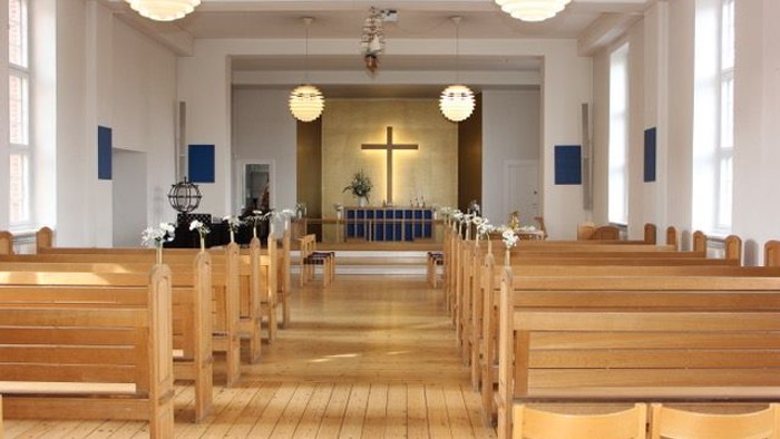 Indre del af kirke med træbænke og lysstake.