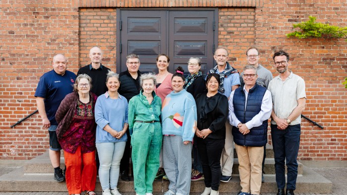 En gruppe af mennesker står sammen udenfor et rødt murværk med en dør.