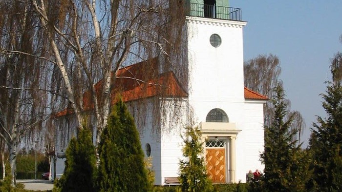 Et hvidt kirke med grøn kuppel og klokketårn, omgivet af træer og buske