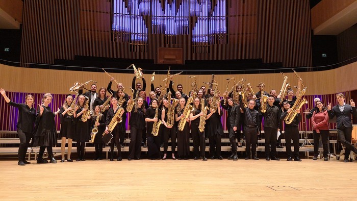 En stor gruppe musiker på scenen med blæserinstrumenter.