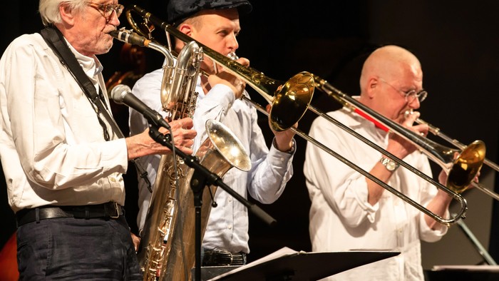 Drei ältere Männer spielen Blechblasinstrumente auf einer Bühne