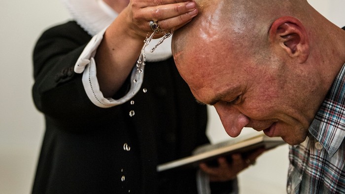 En person holder en andet person i hovedet mens den andet person læser fra en bog