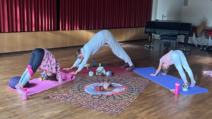 Drei Personen üben Yoga auf bunten Matten in einem Raum