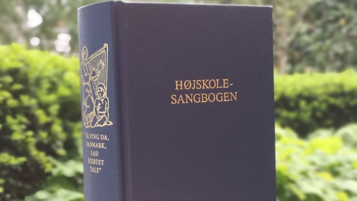 Bog med guldtrykket "Højskole-Sangbogen" på blå bind.