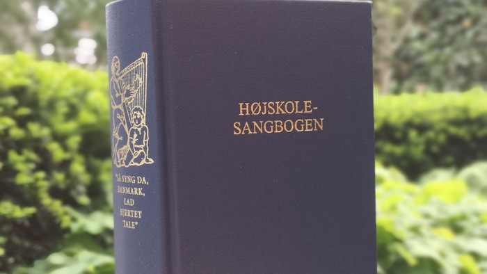 Bog med guldtrykket "Højskole-Sangbogen" på blå bind.