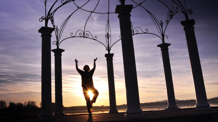 Person steht unter einem filigranen Metallbogen bei Sonnenuntergang