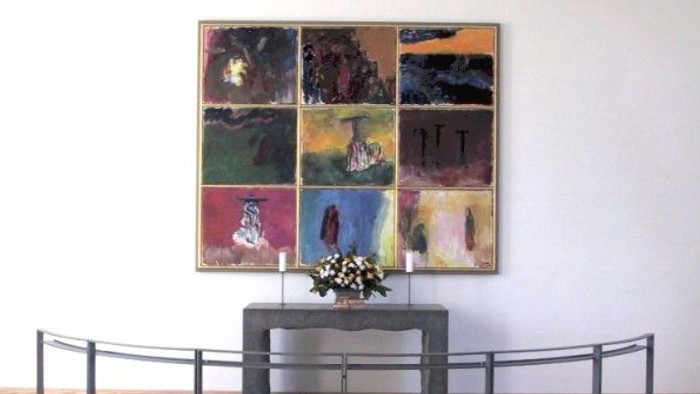 En stor maleriudstilling på væggen med en lille bord med blomster i forgrunden og en kurvet bænke foran