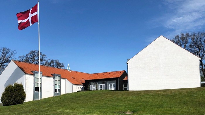 Hvidt hus med rødt tag og dansk flag på en bakke