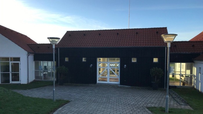 En sort building med røde tag og to lysekøler på en købberstensvej