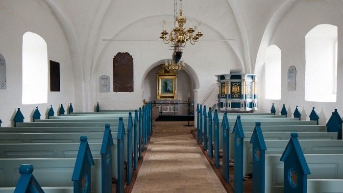 Indre del af kirke med blå bænke og hængende lygter