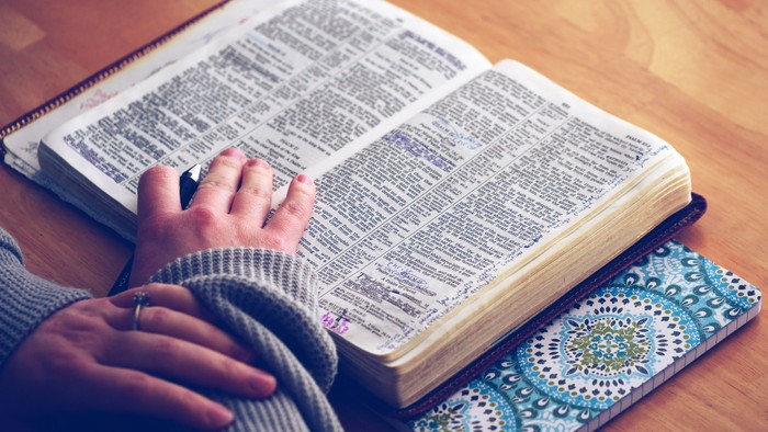 Hands resting on open book with patterned bookmark.