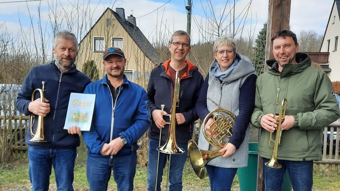 Eine Gruppe von fünf Musikern posiert mit ihren Instrumenten vor einem Haus.