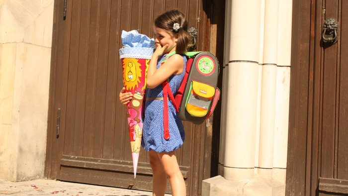 Ein Mädchen mit Rucksack und Luftballon steht vor einer Tür.