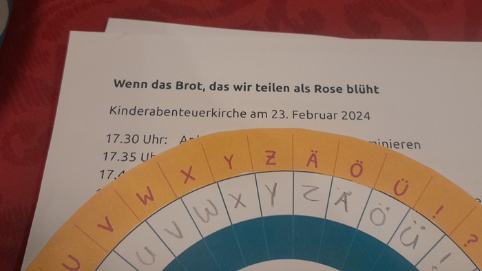 Ein bunter Buchstabering und ein Blatt mit Informationen zur Kinderabenteuerkirche am 23. Februar 2024.
