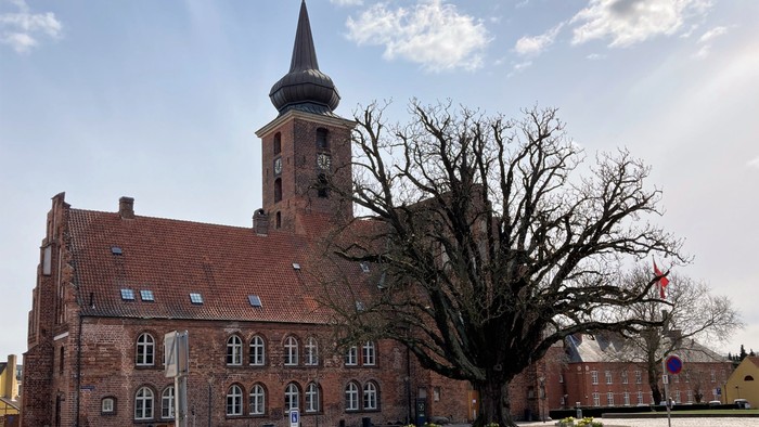 En kirke med klokketårn og en stor træ i forgrunden