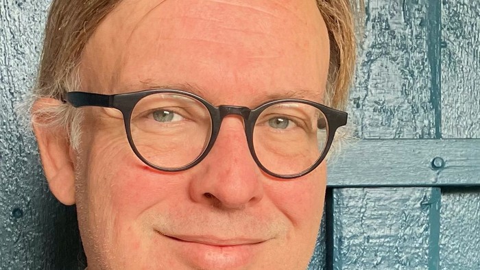 Mand med briller og blå jakke står foran blå dør.