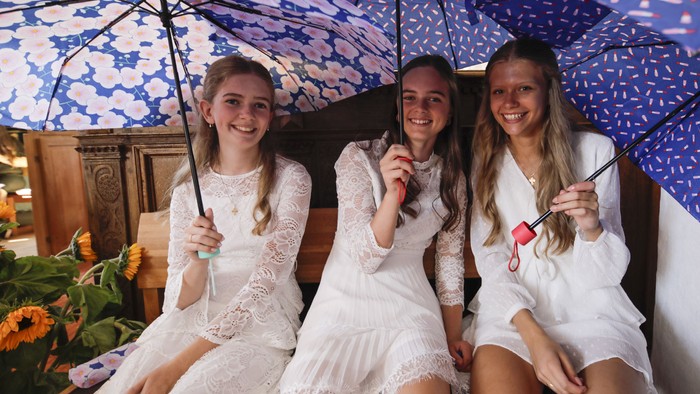 Tre pige i hvidt sitter under blå paraplyer