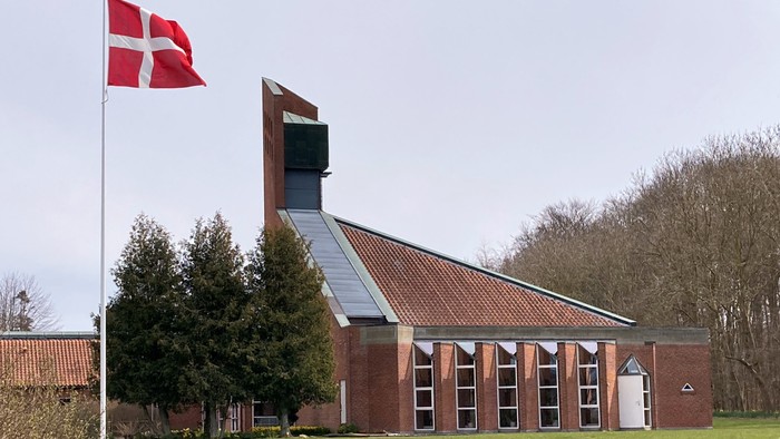 En rød hvid flag ved en kirke med teglmurvade vægge og trætag.