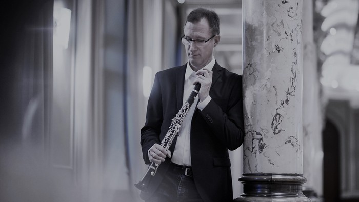 Mann in Anzug spricht in Mikrofon, hält Notenhefter