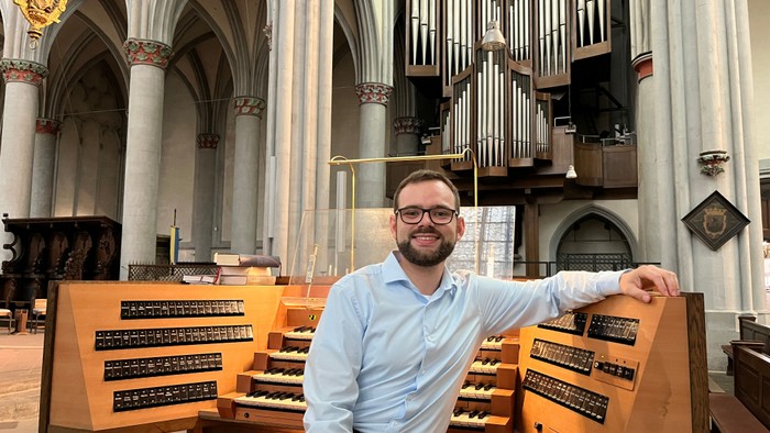 Mann sitzt an Kirchenorgel, lächelt