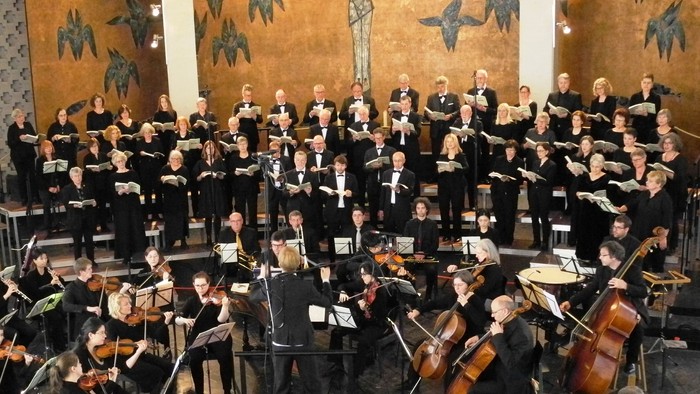 Ein großer Chor und Orchester treten in einer Kirche auf, vor einem Kruzifix.