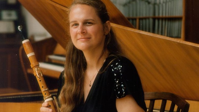 Eine Frau hält eine Flöte und sitzt vor einem Klavier.