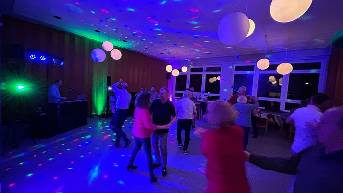 Eine Gruppe von Menschen tanzt auf einer Party unter bunten Lichtern.