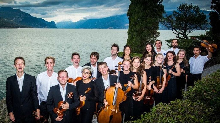 Ein Orchester posiert vor einem See und Bergen