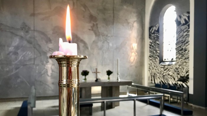 En lysende stearinlys i guldfarvet lysestage i kirke.