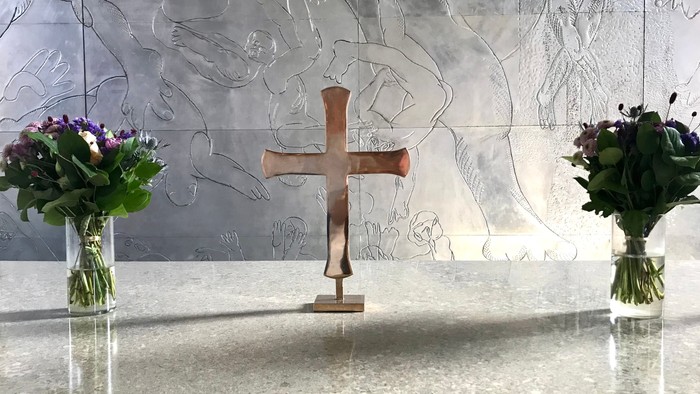 En altertavle med to blomsterstråer og et kors i forgrunden