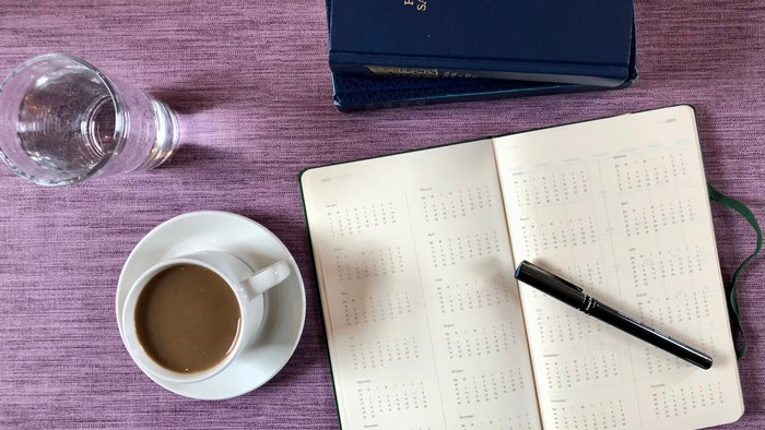 En skriveblok, en kaffe, en pen og en bog på en bord.