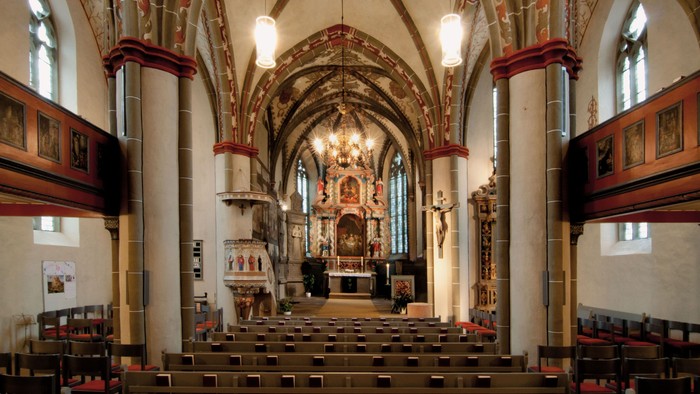 Großer, prunkvoller Kircheninnenraum mit hohen Bögen, Buntglasfenstern und hölzernen Kirchenbänken.