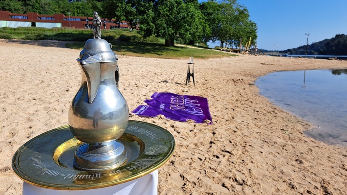 Ein Pokal auf einem sandigen Strand mit einem lila Tuch und einem Stativ im Hintergrund.