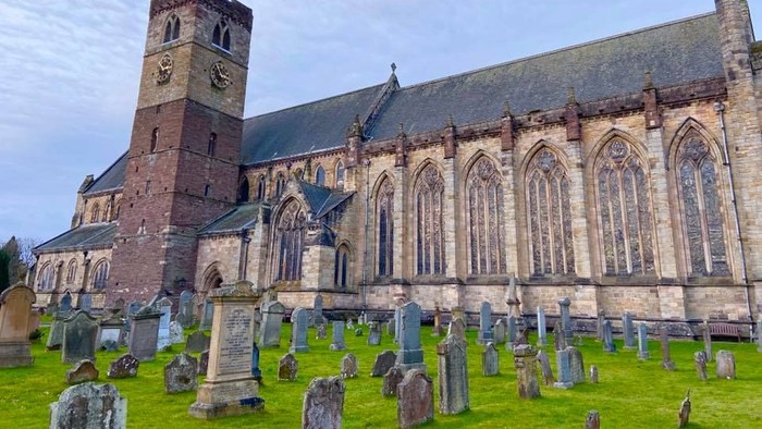 Large historic church with tall tower and numerous arched windows, surrounded by a graveyard.